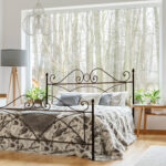 Spacious, cozy bedroom interior with a king-size bed with the grey cushions, lamp and table next to it and the shelves with plants and ornaments on the wall